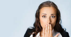 Portrait of surprised excited young business woman covering with hands her mouth, over blue background